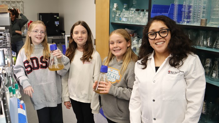 Cristal Zuniga poses with students from Tracy Beach’s Fletcher Hills Elementary class as they visit her SDSU biology lab to learn about microalgae research and STEM opportunities in college.